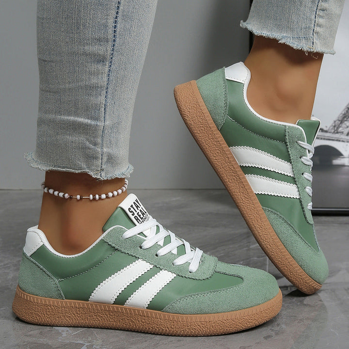 Sage green sneaker with white side stripes, worn on foot