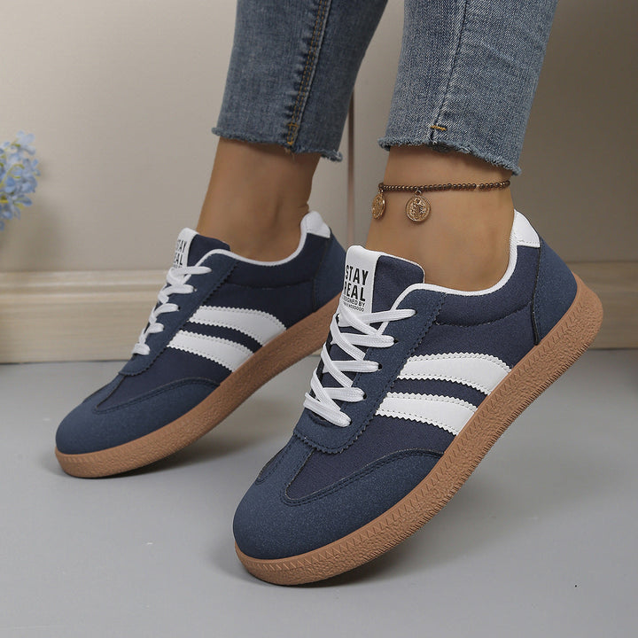 Navy blue low top sneaker with white side stripes, worn on foot