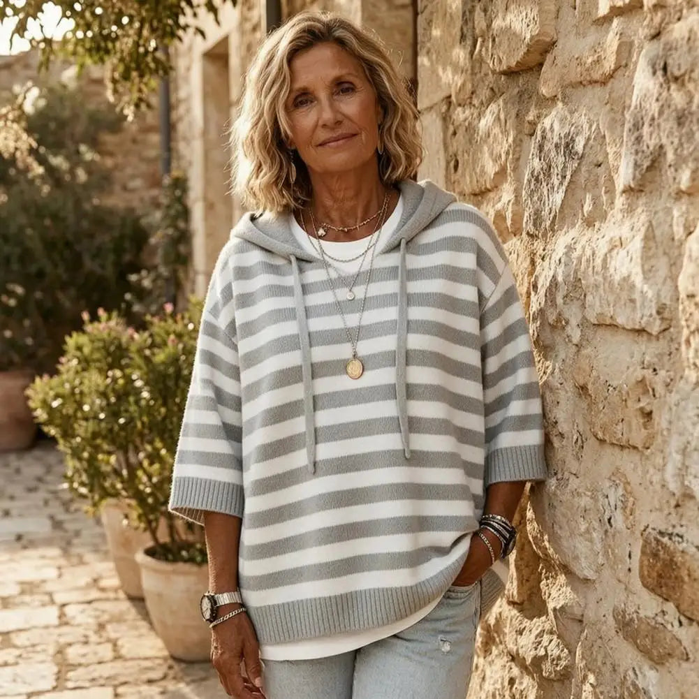 Grey and white striped hooded sweater worn against stone wall