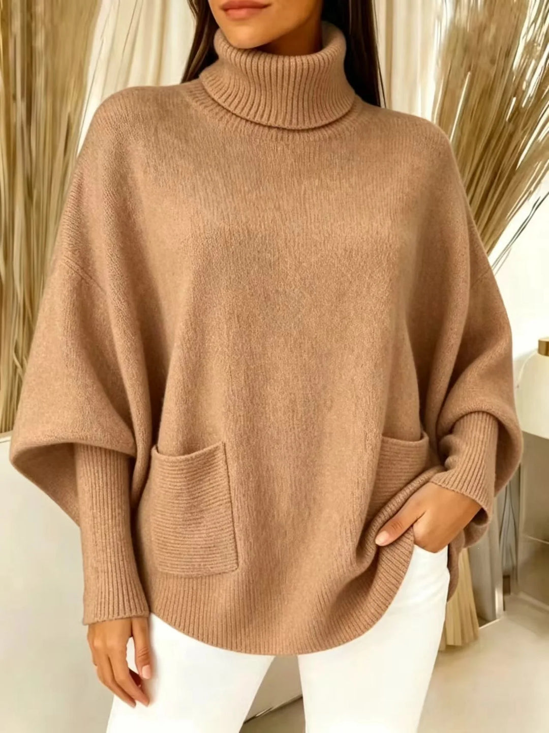 Woman wearing light brown turtleneck batwing sweater with front pocket