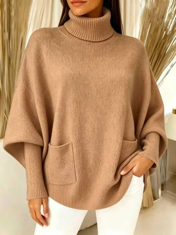 Woman wearing light brown turtleneck batwing sweater with front pocket