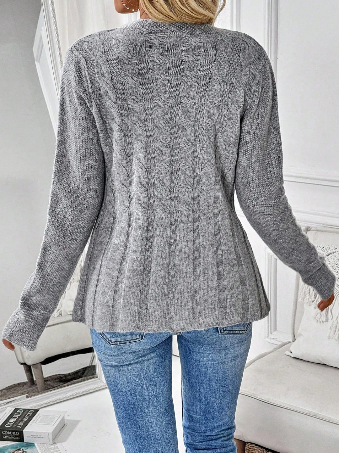 Back view of gray cable knit cardigan showing ribbed pleated hem