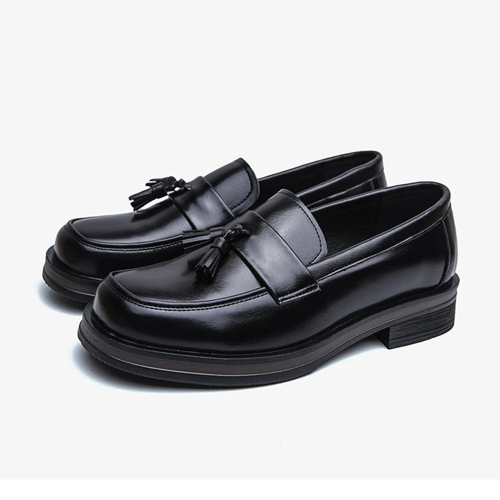 Pair of black tassel loafers on white background