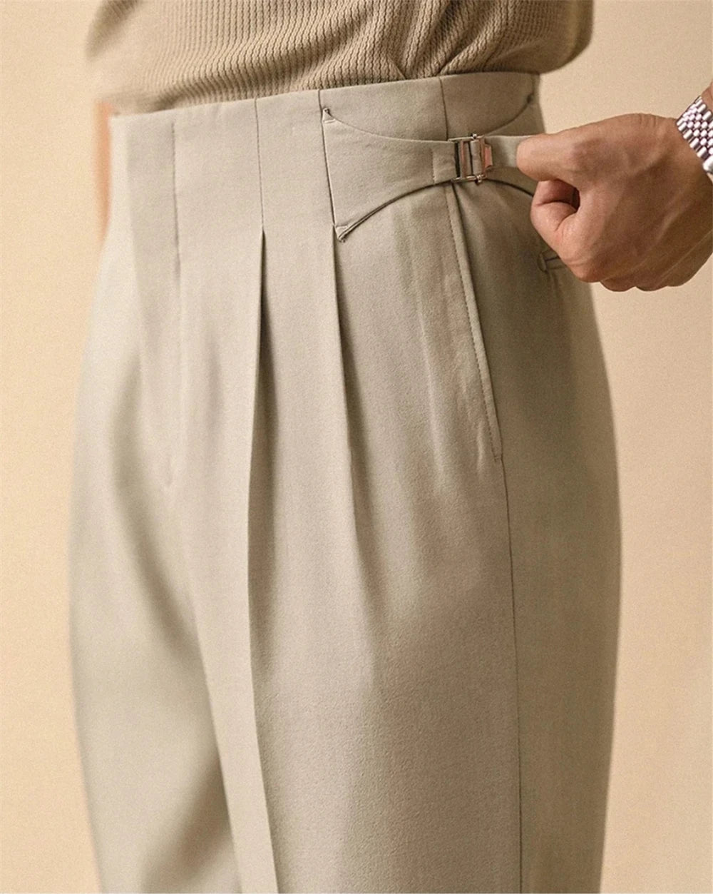 Close up of beige trousers with side tab buckle detail