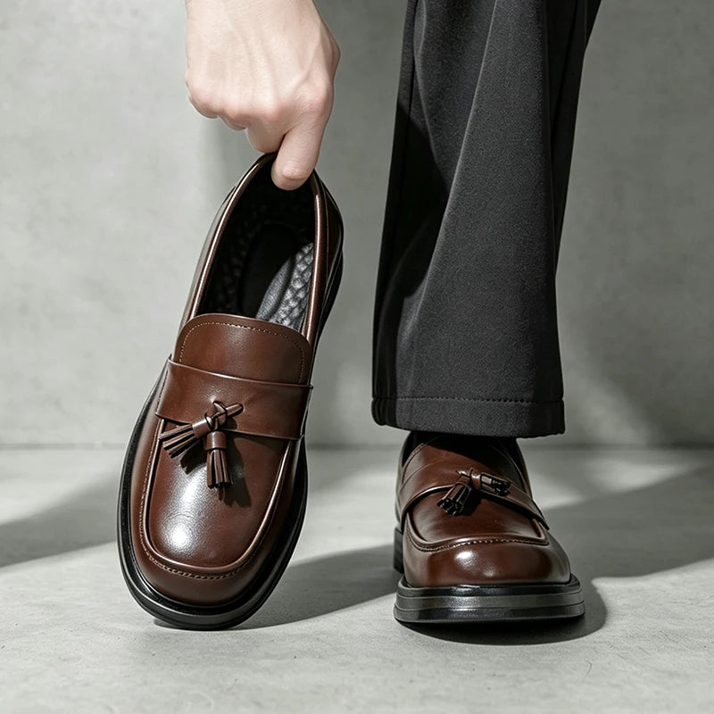 Man holding brown tassel loafer beside foot wearing matching pair