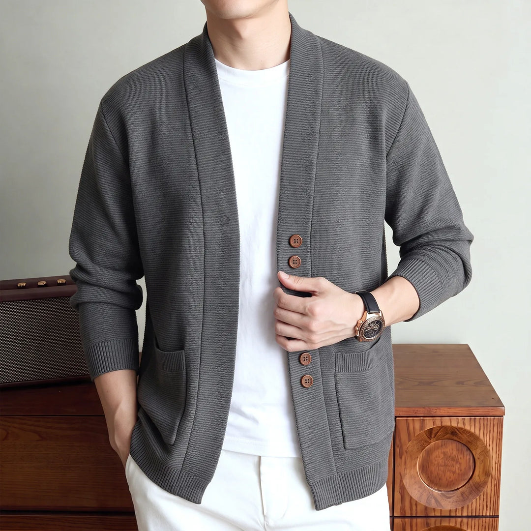 Man wearing gray knit shawl collar cardigan with hands at waist