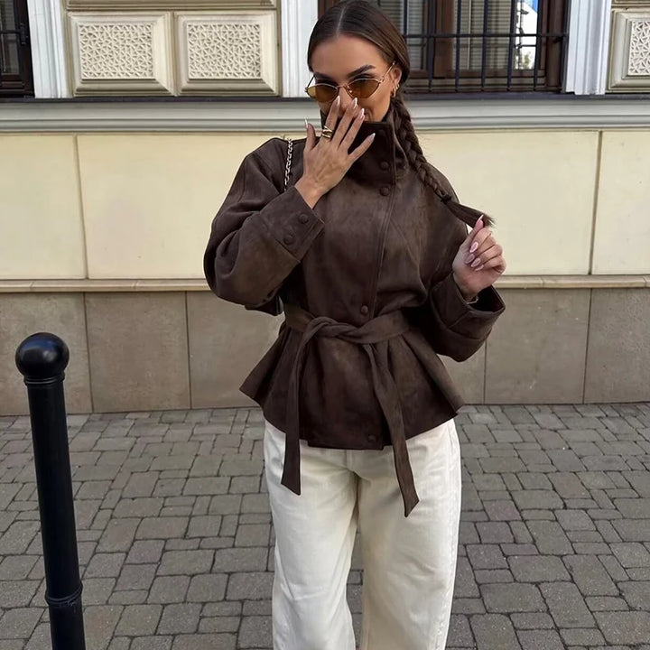 Woman wearing brown belted jacket outdoors with sunglasses