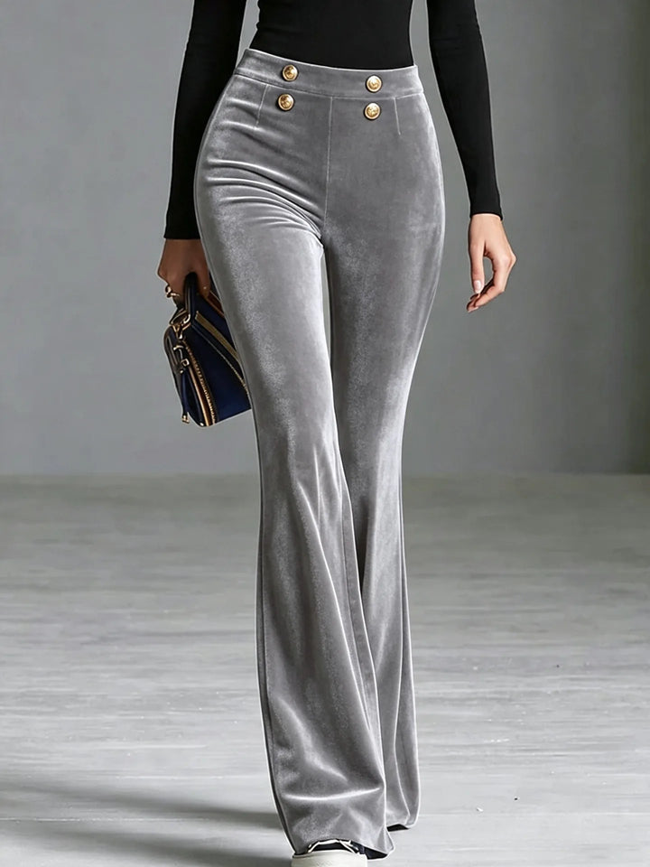 Woman wearing light grey velvet flared high waist pants with gold buttons, front view