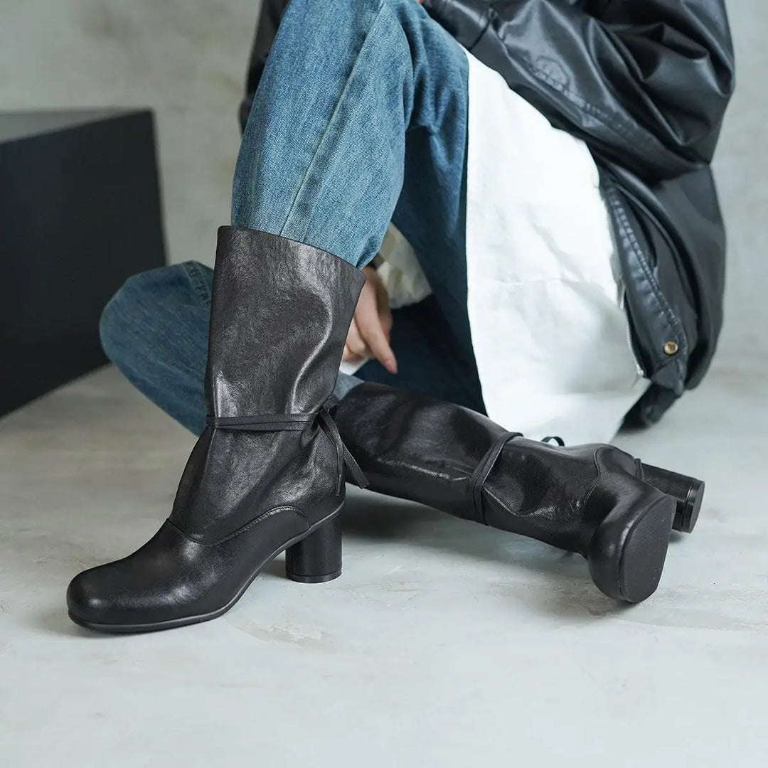Model seated wearing black leather mid-calf boots with ankle tie