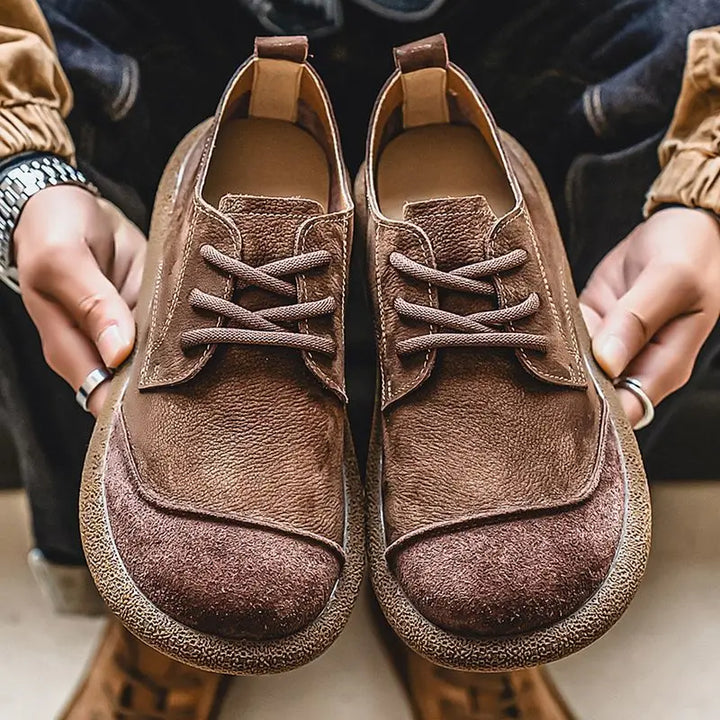 Brown moc toe lace up shoes held in hands, close front view