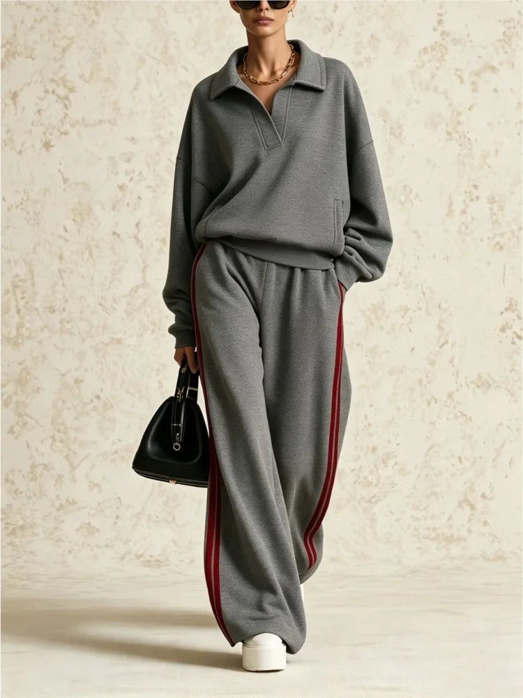 Woman wearing gray two piece collared sweatsuit with red side stripe pants