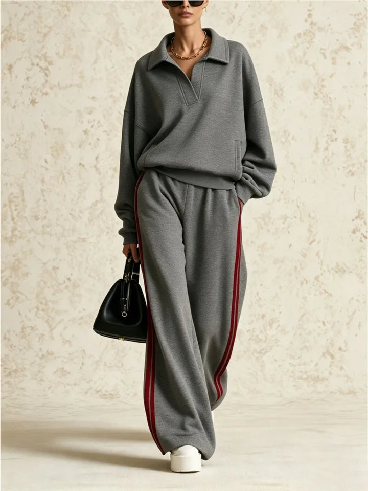 Woman wearing gray two piece collared sweatsuit with red side stripe pants