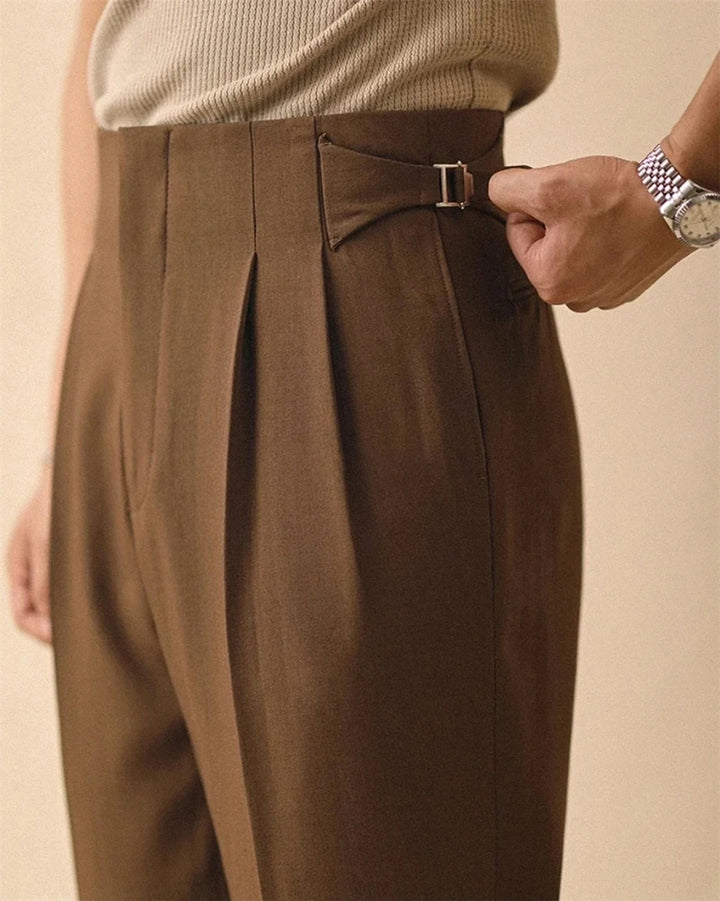 Close up of high waist side tab buckle on brown pleated trousers