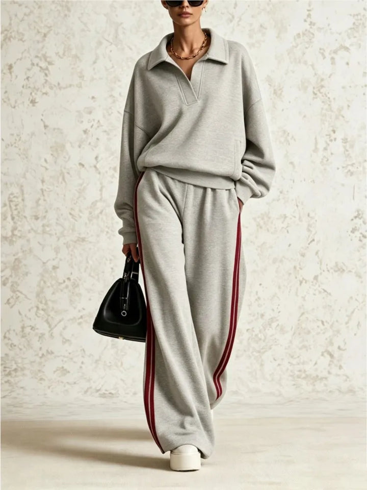 Woman wearing light grey two piece collared sweatsuit with red side stripe pants