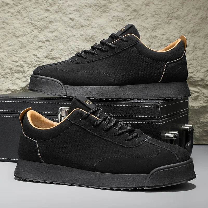 Pair of black low top sneakers shown beside box on stone backdrop