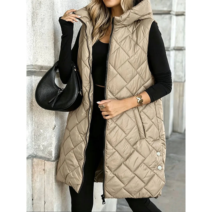 Woman wearing khaki quilted long puffer vest with hood, holding black bag