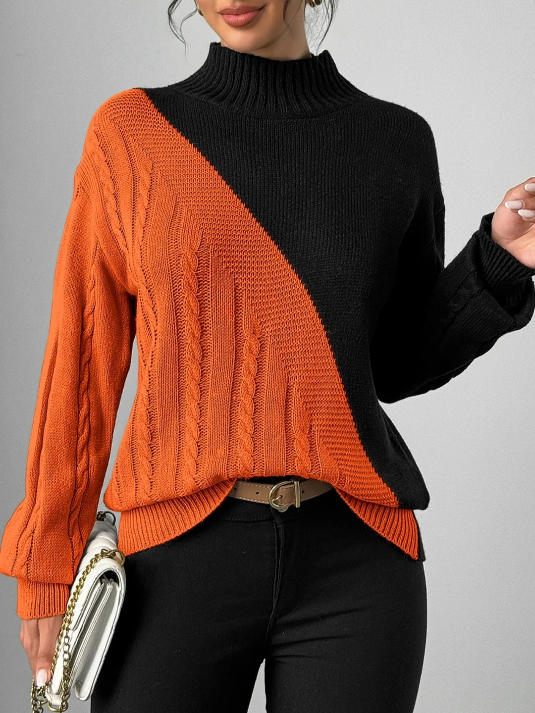 Woman wearing orange and black color block cable knit mock neck sweater, front view