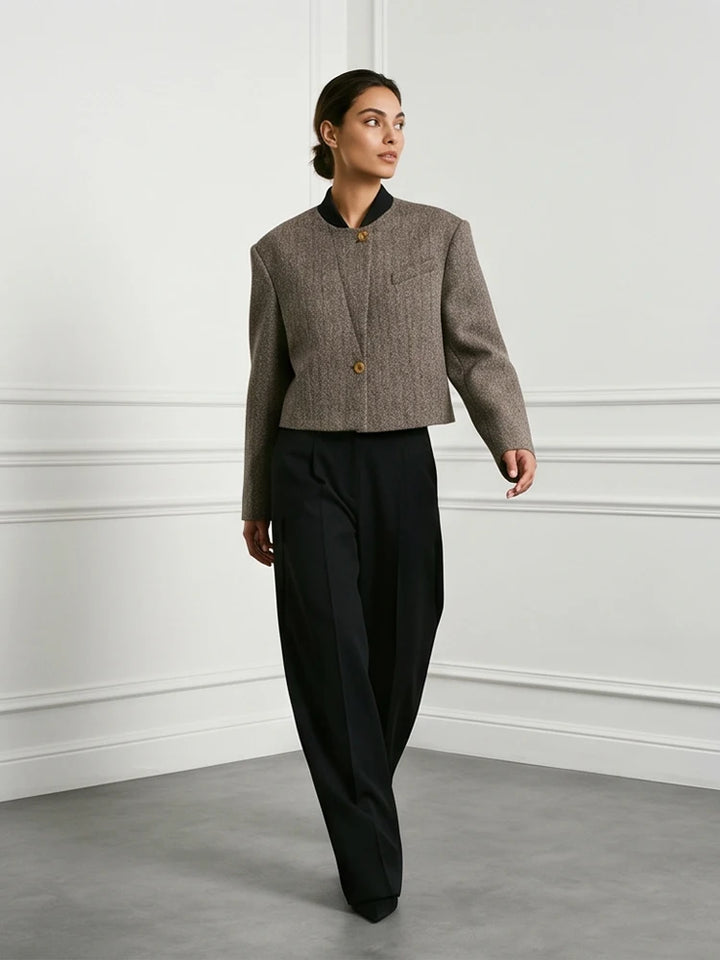 Model walking in grey herringbone cropped jacket and black trousers, three quarter view