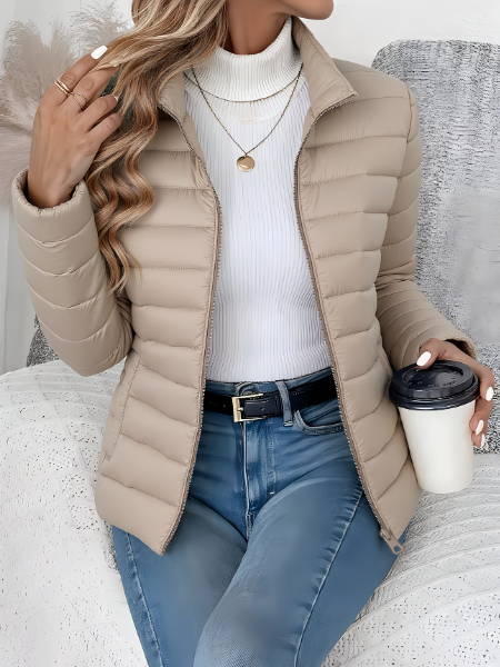 Woman wearing beige quilted puffer jacket with stand collar, holding coffee cup