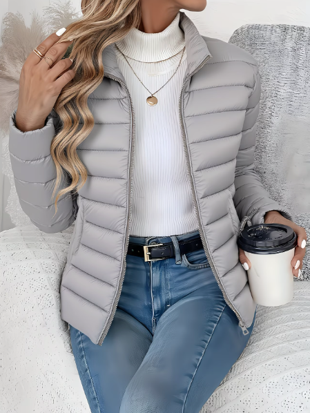 Woman wearing gray quilted puffer jacket with stand collar, holding coffee cup