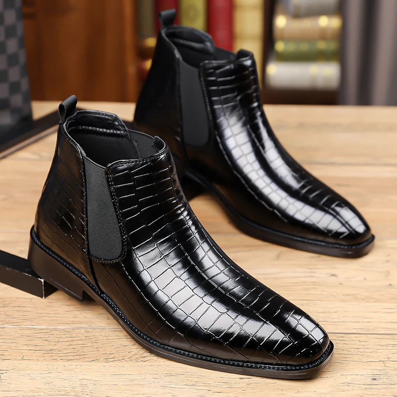 Pair of black croc-embossed Chelsea boots on wood surface