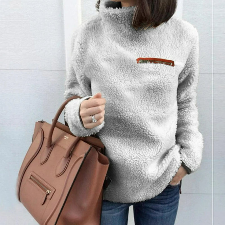 Woman wearing light grey sherpa turtleneck pullover with zip chest pocket