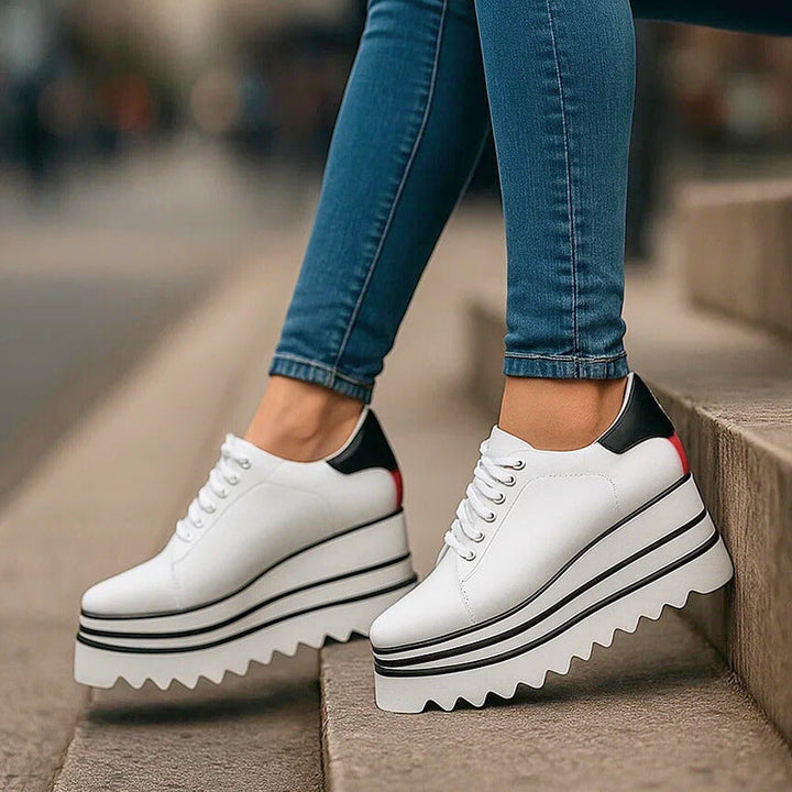 White platform sneakers with black and red heel detail on stairs