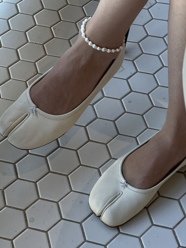 Beige split toe ballet flats on hexagon tile floor with anklet