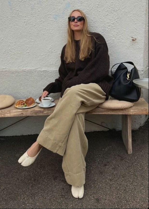 Woman seated on bench wearing beige split toe ballet flats with tan trousers