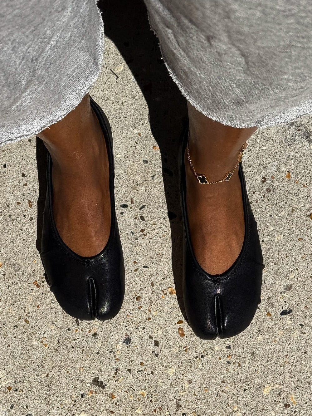 Model wearing black split-toe flats with anklet