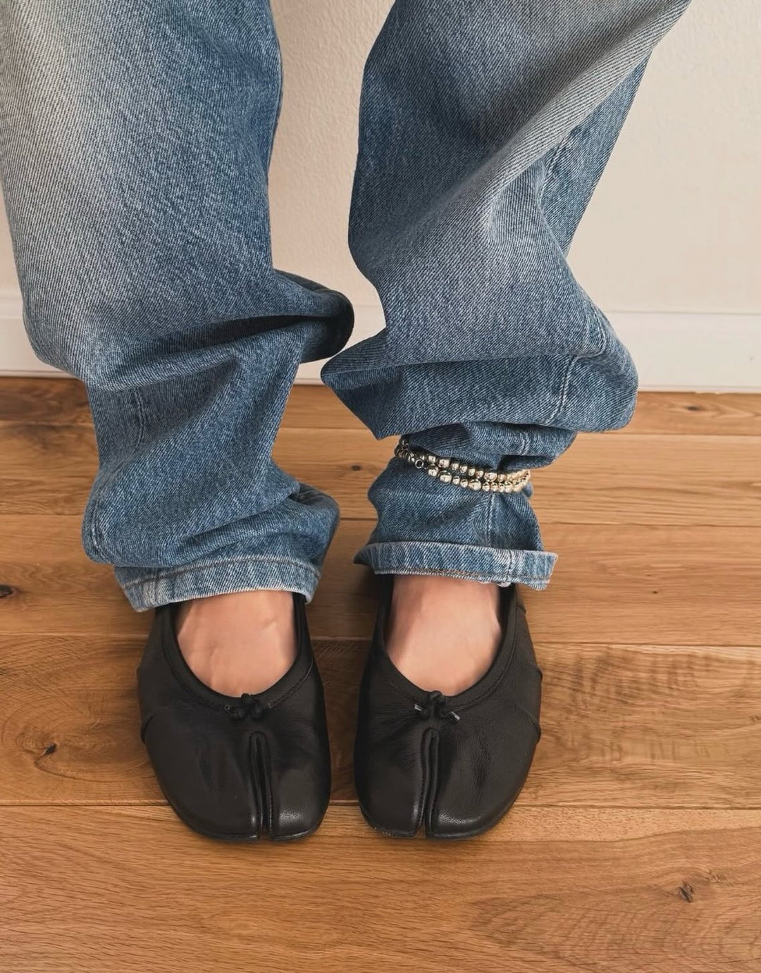 Model wearing black split-toe flats with cuffed jeans