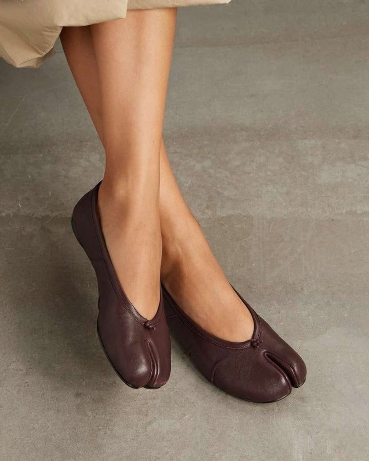 Model wearing burgundy split-toe flats, crossed ankles