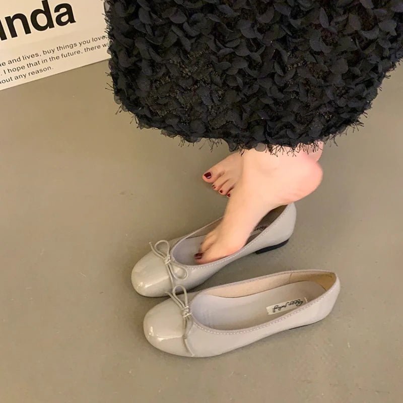 Gray patent ballet flats with bow detail on floor