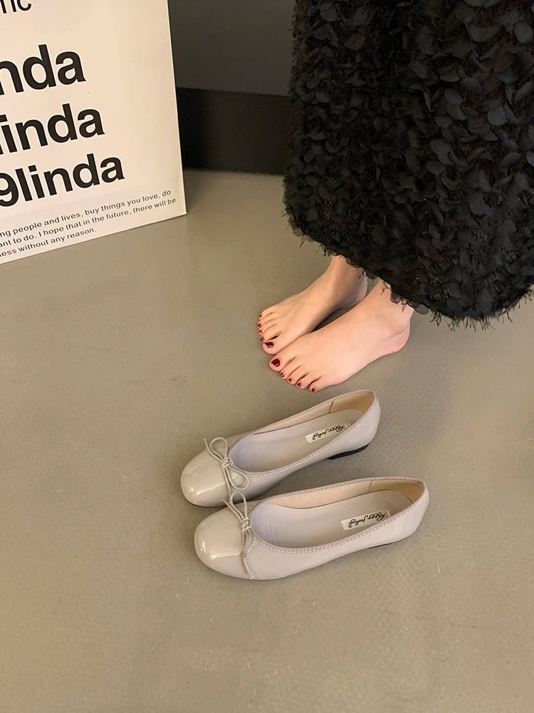 Gray patent ballet flats with bow detail near bare feet
