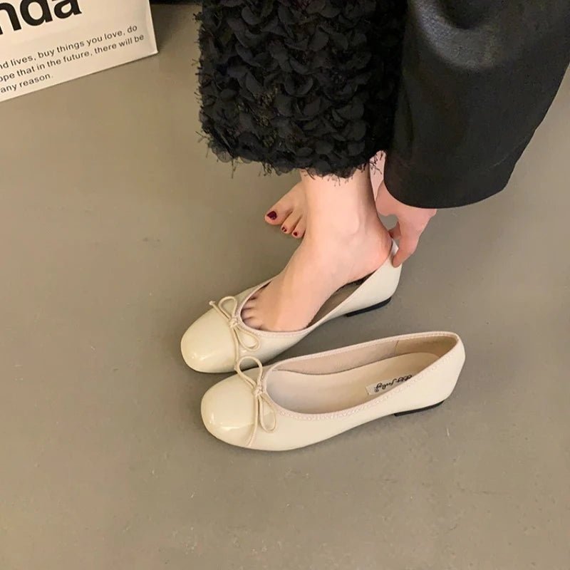 Beige patent ballet flats with bow worn near black skirt