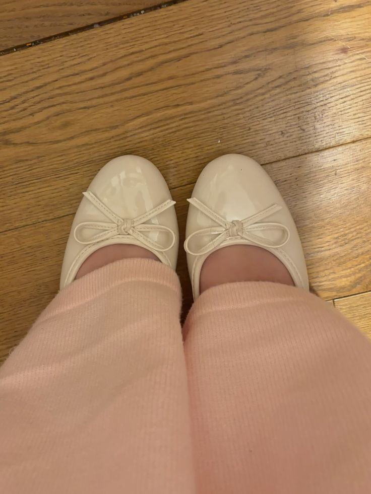 Beige patent ballet flats with bow detail worn on feet