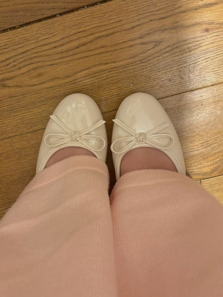 Beige patent ballet flats with bow detail worn on feet