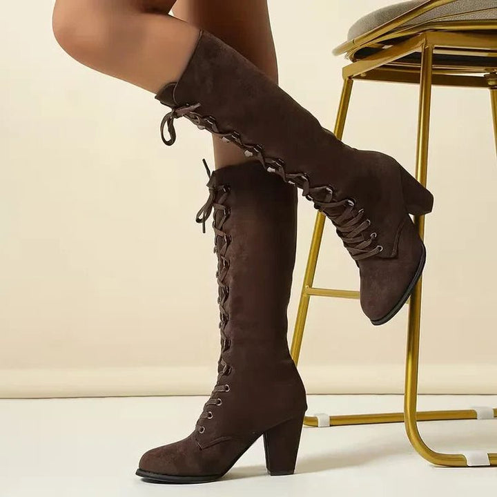 Model wearing brown lace-up knee high boots seated near stool